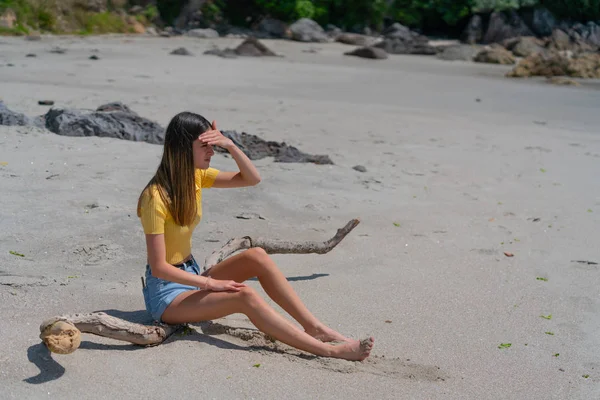 Teenage girl in yellow top and denim shorts sitting on piece of — Stock Photo, Image