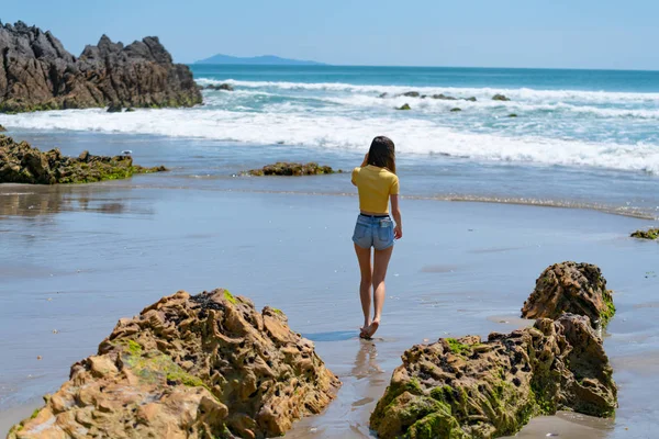 Young woman in bright yellow top walking near waters edge — Stock Photo, Image