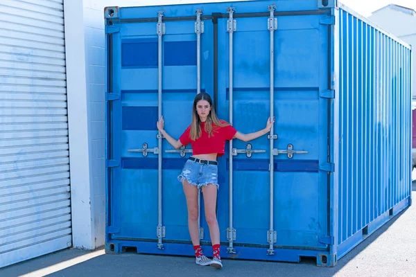 Pretty girl in red top and tatty denim shorts standing by cargo — ストック写真