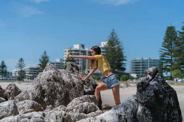 Teenage girl in yellow top and denim short pants climbs rocks — Stock Photo, Image
