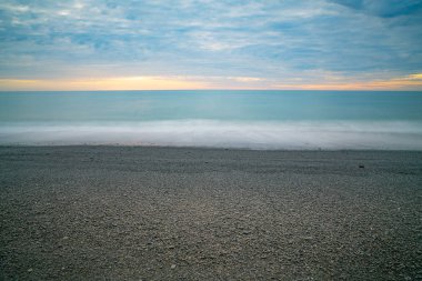 Güneş doğarken dramatik bulutlu gökyüzünün altında gri taşlı plaj.