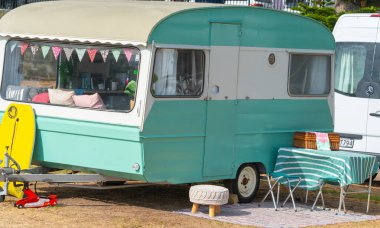 Tauranga, Yeni Zelanda - 20 Şubat 2020; Retro tarzı yeşil ve beyaz karavan, dışarıda sarı gövde ve mobilya ile yaz tatili için hazırlanıyor.