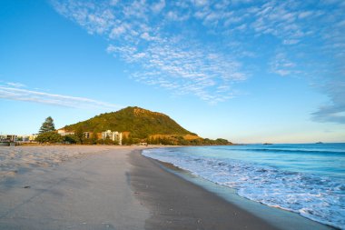 Güneşin doğuşuyla birlikte Maunganui Dağı 'nın ana plajında kumlu bir sahil..