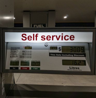 Pompa dolabının önündeki benzin istasyonunda aydınlatılmış self servis tabelası..