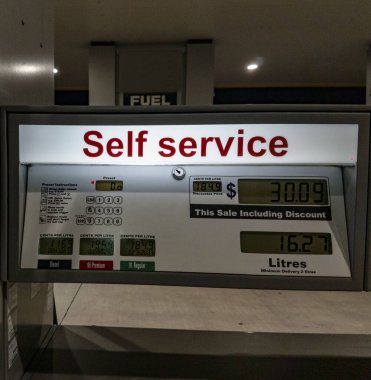 Illuminated self-service sign at gas station on front of pump cabinet. clipart