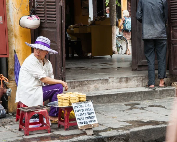 越南海安2013年10月17日 一位戴着现代帽子的女街头摊贩坐在一幢用托盘出售蛋糕的大楼门外的凳子上 — 图库照片