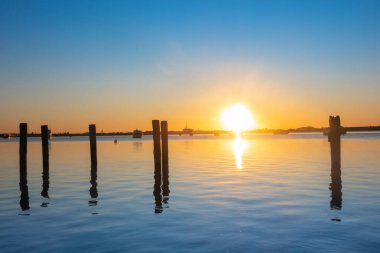 Tauranga Limanı 'nda gündoğumları sakin sular ve sabah ışığında siluetlenmiş eski karakollar..