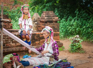 Bagan Myanmar - 29 Ekim 2013; Biri boyunlarında pirinç halkalar olan iki Kayan kadın, diğeri ise seçici bir odak duvarında oturup.