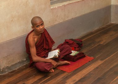 Bagan Myanmar - 30 Ekim 2013; Birmanyalı Budist Keşiş ahşap zeminde tek başına otururken kafasını kaldırıp incelerken,.