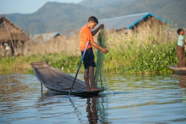 Inle Gölü Myanmar - 2 Kasım 2013; İnsan geleneksel uzun sopasında, yeşil su otunun balık ağını kaldırdığı kanal arasında duruyor,