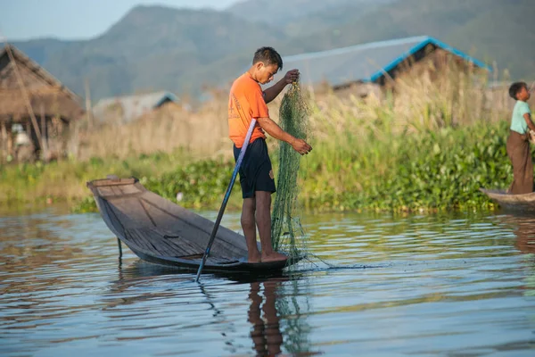 Inle Gölü Myanmar - 2 Kasım 2013; İnsan geleneksel uzun sopasında, yeşil su otunun balık ağını kaldırdığı kanal arasında duruyor,