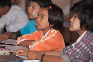 Inle Gölü Myanmar - 3 Kasım 2013; Kız okulda oturuyor, dikkatle ileriye bakıyor ve her iki tarafta da dikkati dağılmış bir erkekle izliyor..