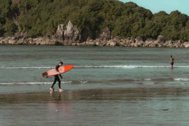Maunganui Dağı Yeni Zelanda - 9 Mayıs 2020; Vintage efekt sörfçüsü turuncu sörf tahtası taşıyan suyu bırakıyor.