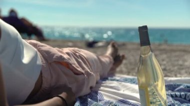 Fransız Riviera 'sında şaraplı kadın. Güney Fransa 'da dalgalar arkadan vururken bir kadın sahilde bir şişe şarapla soğuyup rahatlıyor..
