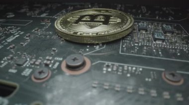 Bit Coin Circuit Board. Wide macro lens, extreme close up (ECU) over a black circuit board as it rotates around and stops on a golden bitcoin medallion with a capital B () symbol and circuit design.