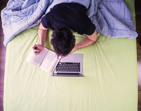 Studera eller arbeta i sängen, noterar från laptop, lätt helgen studie — Stockfoto