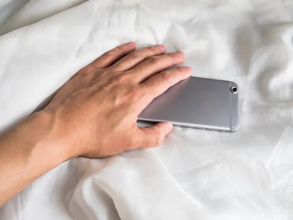 Mano buscando teléfono en la cama, edredón blanco —  Fotos de Stock