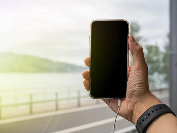 Phone hand holding with ear phone plugged in, and road view