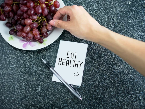 Eat Healthy text on paper note with hand picking grape — Stock Photo, Image