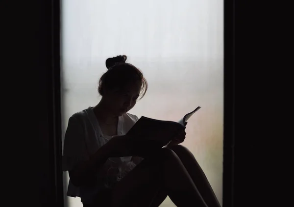 Vintage filtrado na silhueta da menina sentada no livro de leitura da janela — Fotografia de Stock