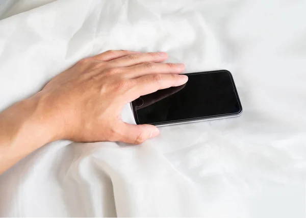 Mano tocando el teléfono inteligente en la cama, edredón blanco —  Fotos de Stock