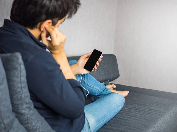 Man listen to music from phone using earphone on sofa