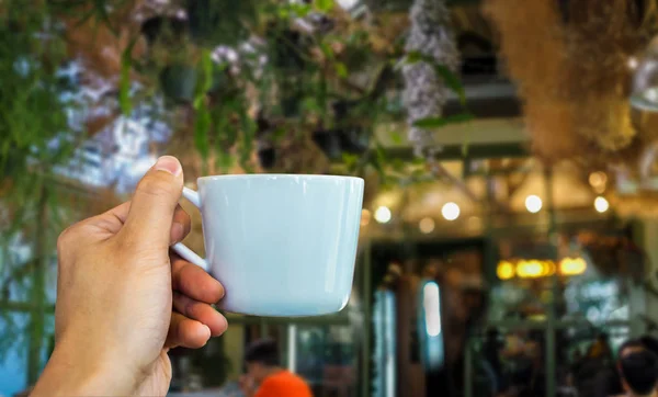 Coffee cup on hand holding with garden cafe view