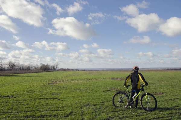 Homem com uma bicicleta em um campo verde — Fotografia de Stock