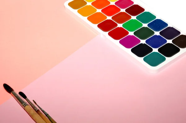 Aquarellfarben mit Pinseln auf rosa Hintergrund, Draufsicht — Stockfoto