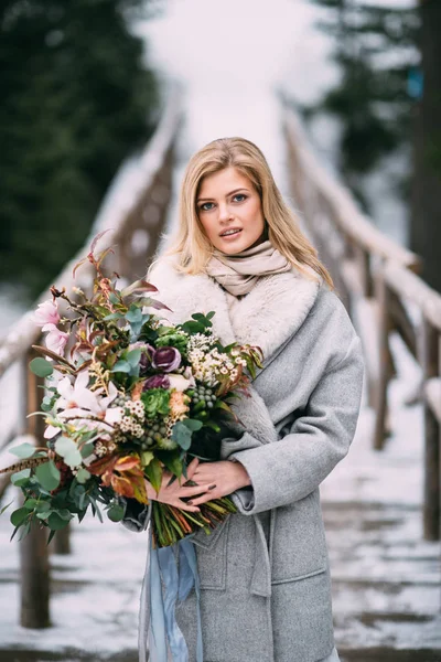 Menina bonita fica no inverno com um buquê de flores em suas mãos — Fotografia de Stock