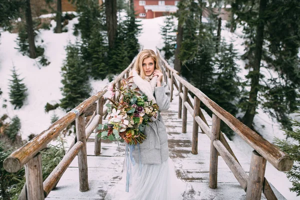 Hermosa joven se para en invierno con un ramo de flores en sus manos — Foto de Stock
