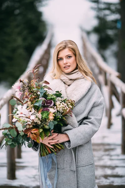 Mooi jong meisje staat in de winter met een boeket bloemen in haar handen — Stockfoto