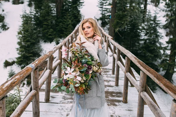 Hermosa joven se para en invierno con un ramo de flores en sus manos — Foto de Stock