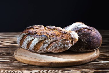 Fırından yeni çıkmış bir yuvarlak ahşap plaka üzerinde siyah bir arka plan üzerinde ev yapımı ekmek yalan.