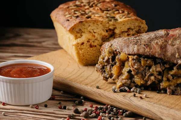 Muffin à la citrouille et rouleau de viande cuit au four avec garniture et sauce sur une assiette en bois sur fond noir — Photo