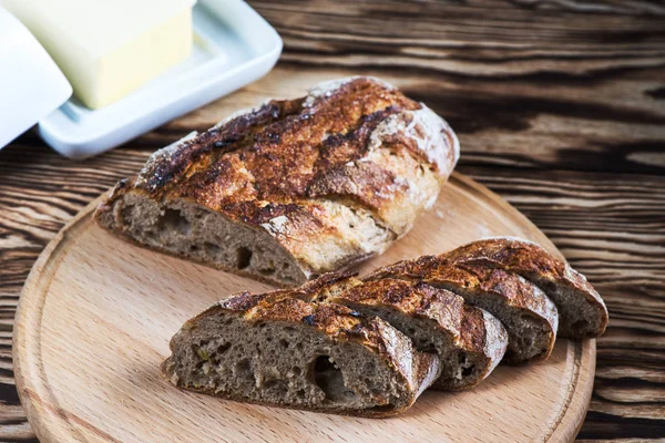 Frisch gebackenes hausgemachtes Brot liegt auf einem runden Holzteller auf schwarzem Hintergrund.. — Stockfoto