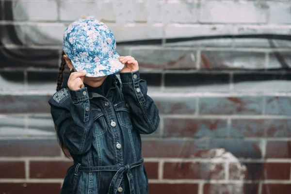 Niedliches kleines Mädchen in Jeans Strickjacke und auf Roller auf dem Hintergrund die städtische bunte Wand — Stockfoto
