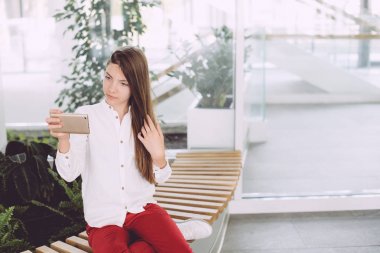 Bir bankta oturan bir şehir caffe içinde bir akıllı telefon kullanan mutlu kız. Bir genç kız ile bir smartphone onun elinde bir kafede zaman harcıyor