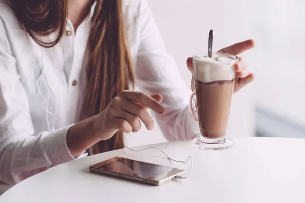 Beautiful brunette drinking coffee on summer terrace. A teenage girl with a smartphone in her hands spends time in a cafe