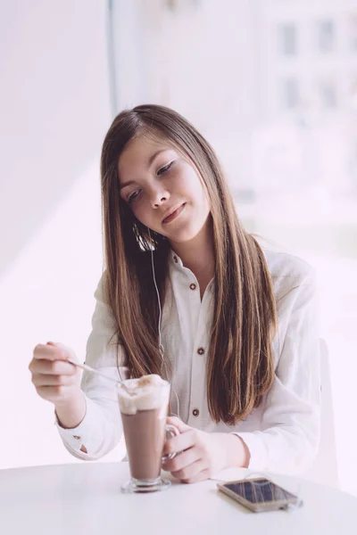 Beautiful brunette drinking coffee on summer terrace. A teenage girl with a smartphone in her hands spends time in a cafe