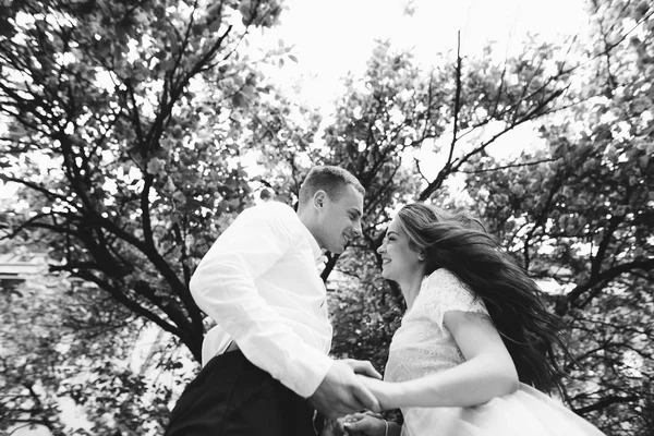 Feliz joven pareja enamorada disfruta del día de primavera, hombre amoroso sosteniendo en las manos a su mujer sin preocupaciones caminando por el parque — Foto de Stock