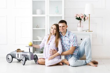 Bir erkek ve hamile bir kadın birlikte zaman geçirir, elmayı tutar ve yerde otururlar. Güzel, parlak misafir odası