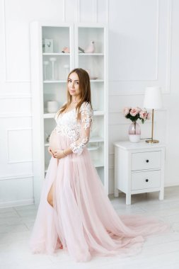 Beyaz saçlı, bebek bekleyen genç, güzel bir elbiseyle odanın ortasında duran güzel bir kadın. Annelik
