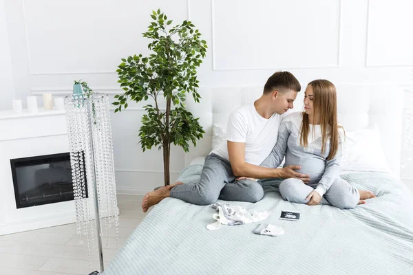 Young couple - man and woman expecting baby, looking at baby clothes and photo. Awaiting the birth of a baby — Stock Photo, Image