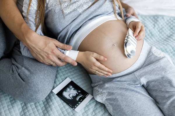 Young couple - man and woman expecting baby, looking at baby clothes and photo. Awaiting the birth of a baby — Stock Photo, Image