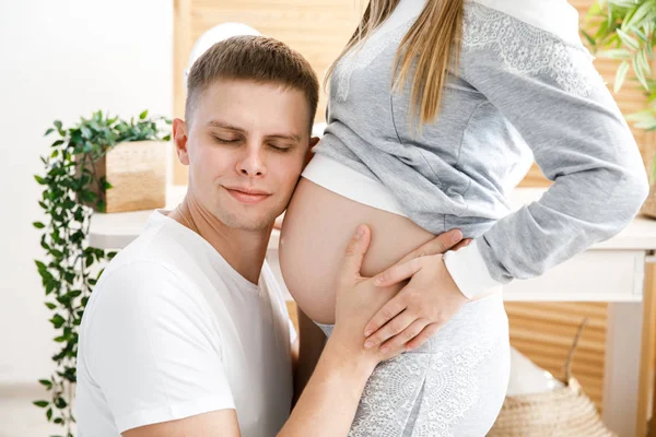 Casal jovem - homem e mulher esperando um bebê, passar o tempo juntos, marido abraça a barriga e beijos de sua esposa. Esperando o nascimento de um bebê — Fotografia de Stock