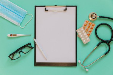 Doctor's desk top view. Stethoscope, pills, glasses and notebook on a colored background.