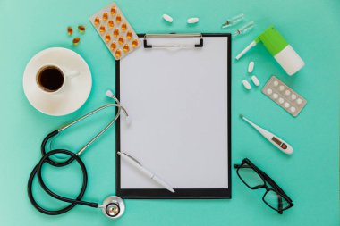 Doctor's desk top view. Stethoscope, pills, glasses and notebook on a colored background.