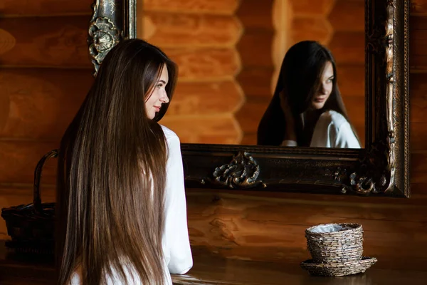 Young woman in a robe brushing her long dark-blond hair after getting up in the morning.