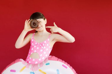 Stüdyoda elinde donutla ve lastik yüzükle poz veren mayolu sevimli küçük bir kız resmi. Havada yüzen güzel bir kız çocuğu.